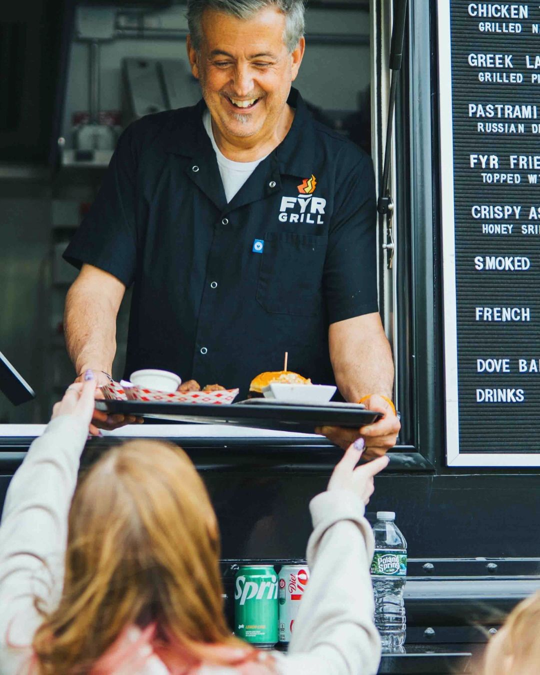 Food truck staff handing a finished order to a customer at the service window